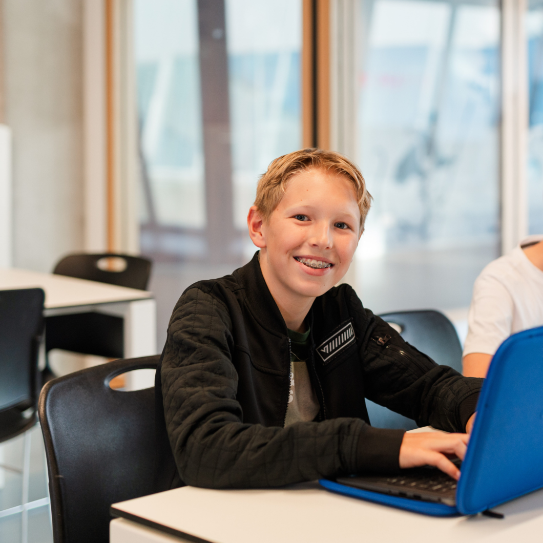 Jongen zittend in de klas met een laptop voor zich.