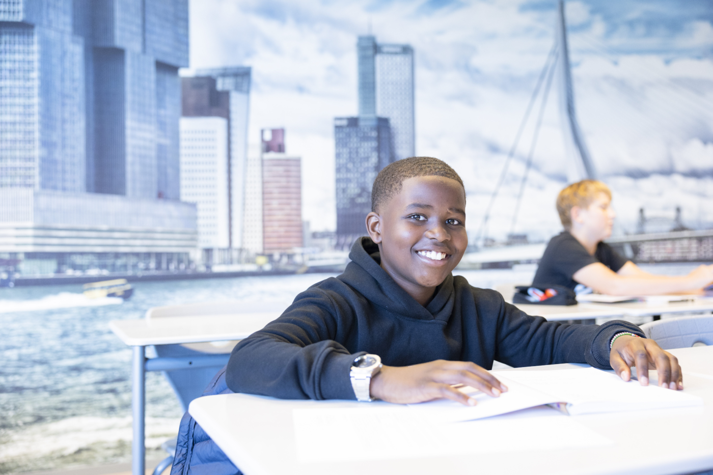 Leerling van Melanchthon Mavo Schiebroek zittend in de klas. Op de achtergrond een foto van Rotterdam.